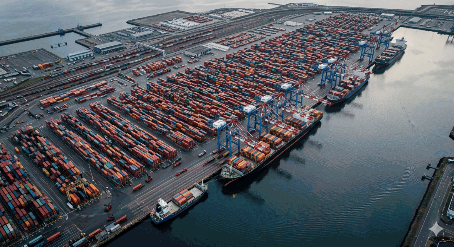 Massive container port terminal from above — thousands of colourful shipping containers and gantry cranes loading vessel